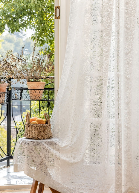 a window with a white curtain and a basket of fruit